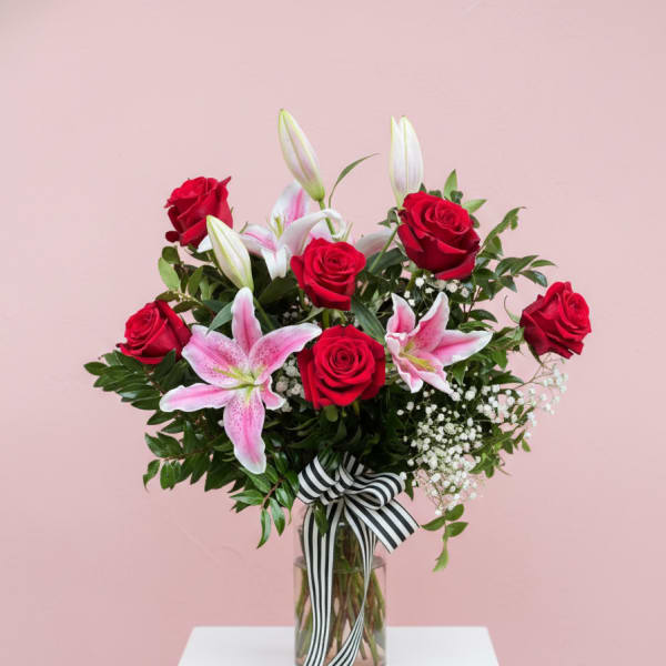 Red roses and pink lilies in a glass vase with a striped ribbon