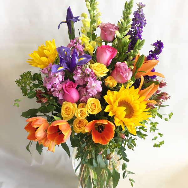 Colorful mixed bouquet in a clear glass vase with sunflowers, roses, tulips, and irises