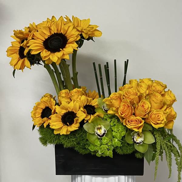 Yellow sunflowers and roses arranged in a black rectangular container