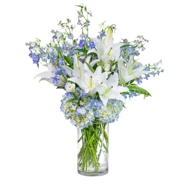 Tall glass vase of white lilies, blue hydrangeas, and blue delphinium in a layered arrangement