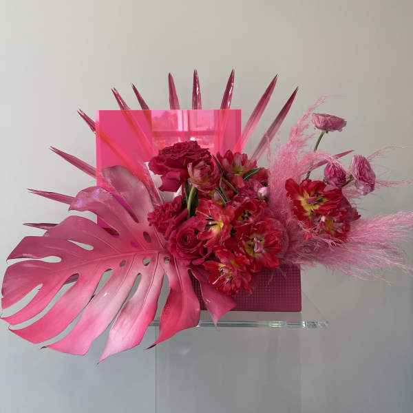 Pink floral arrangement with tropical leaves and a clear vase