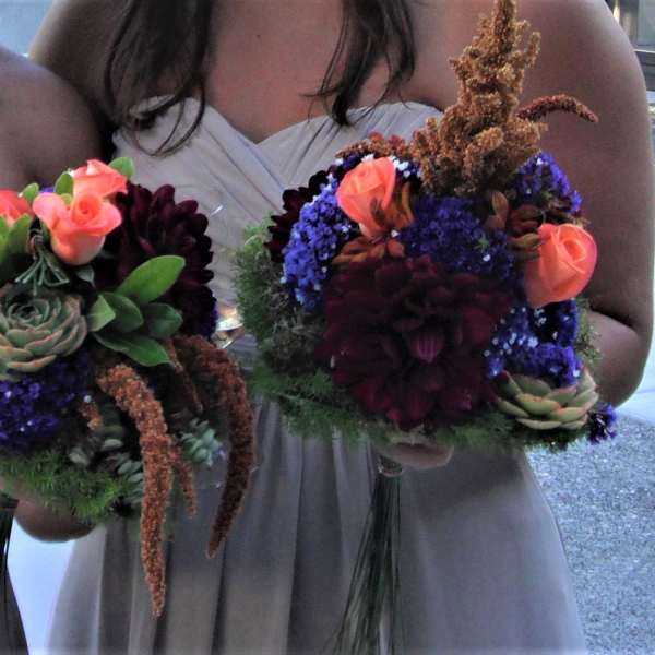 Two bridesmaids hold bouquets with succulents, coral roses, and dark blooms.