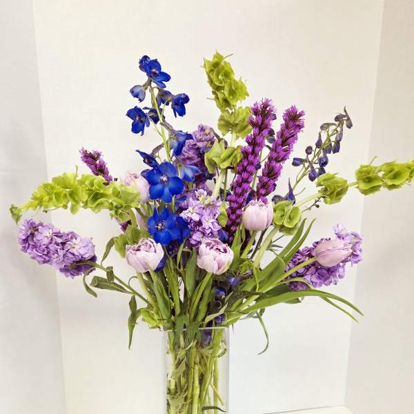 Tall vase arrangement with blue, purple, and pale pink flowers