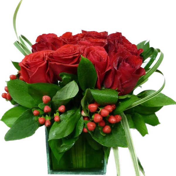Red roses in a square glass vase with green foliage and red berries