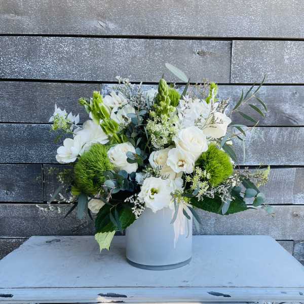 White floral arrangement in a white vase with bright green accents