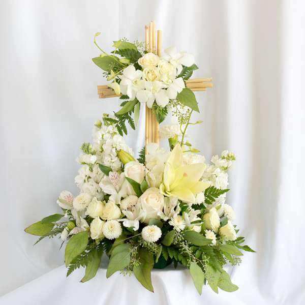 White floral arrangement on a wooden cross with lilies and roses