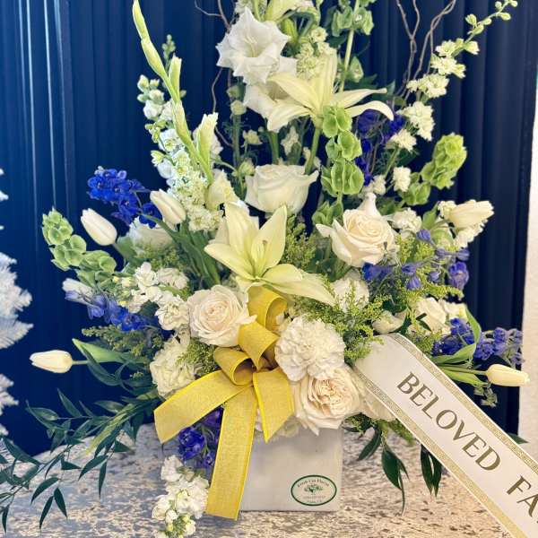 Tall floral arrangement with white lilies, roses, and blue flowers in a vase