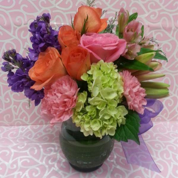 Mixed bouquet of roses, carnations, hydrangea, and purple blooms in a glass vase