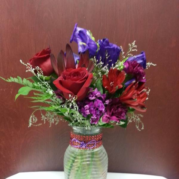 Mixed bouquet of red, purple, and blue flowers in a glass vase