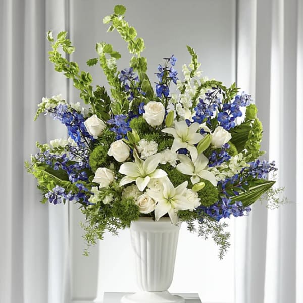 White lilies and roses in a white pedestal vase with blue flowers