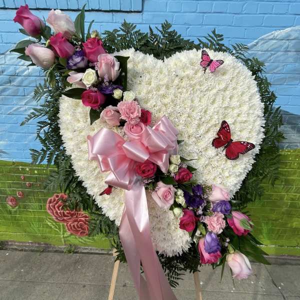 Heart-shaped white floral spray with pink and purple roses and ribbon
