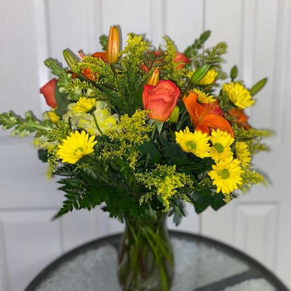 Bouquet of orange roses, yellow daisies, and lilies in a glass vase