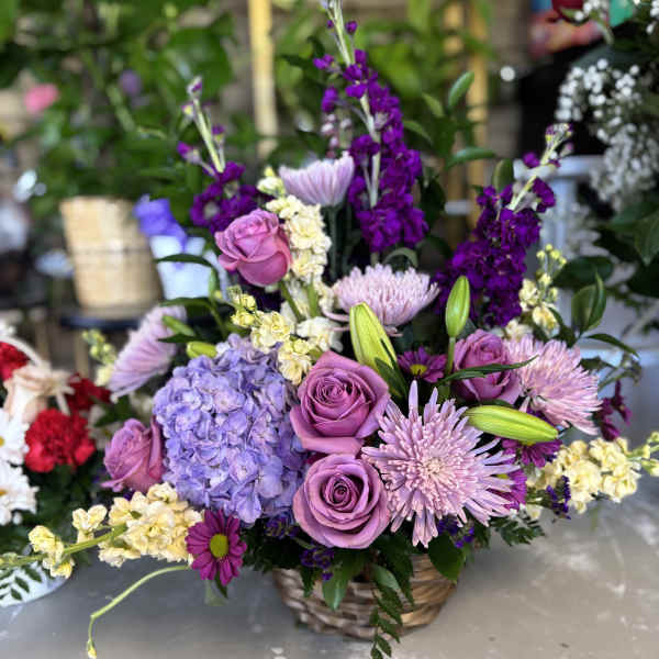 Lavender roses and purple flowers arranged in a wicker basket