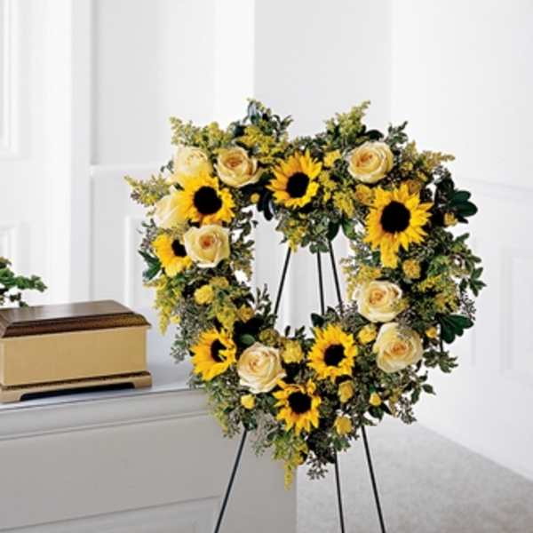 Heart-shaped floral wreath with sunflowers and cream roses on a stand