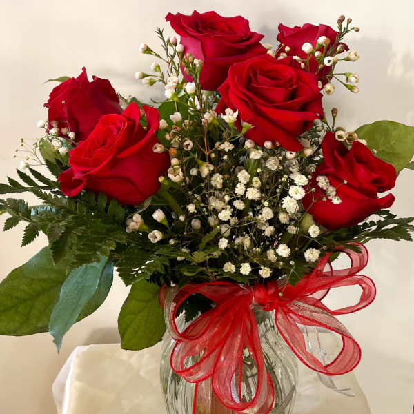 Bouquet of red roses and white baby's breath in a clear glass vase with a red ribbon