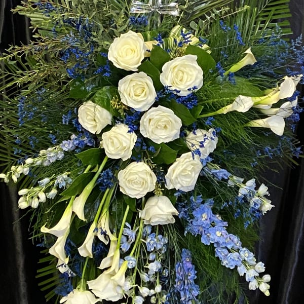 Standing spray of white roses and calla lilies with blue flowers and a glass cross.