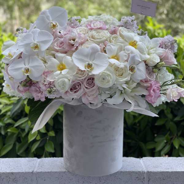 White orchids and blush roses arranged in a tall gray vase
