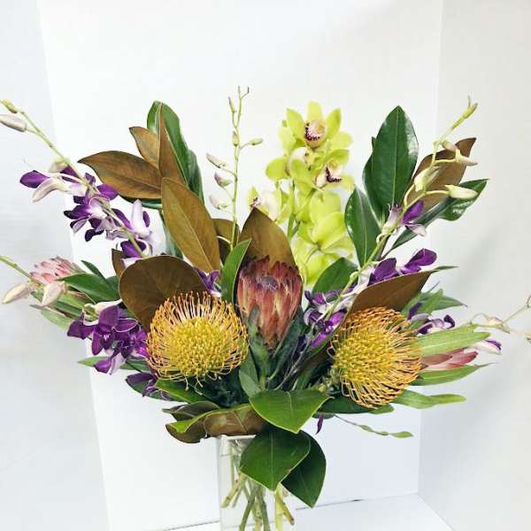 Tropical bouquet with orchids and protea in a clear glass vase