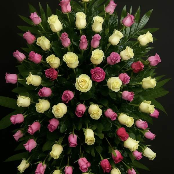 Tall standing spray of pink and pale yellow roses arranged on lush dark foliage