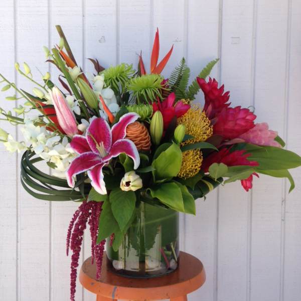 Tropical bouquet with pink lily, red blooms, and orchids in a glass vase