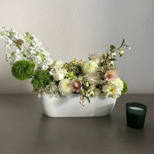 White floral arrangement in a low rectangular vase with green pom-pom accents