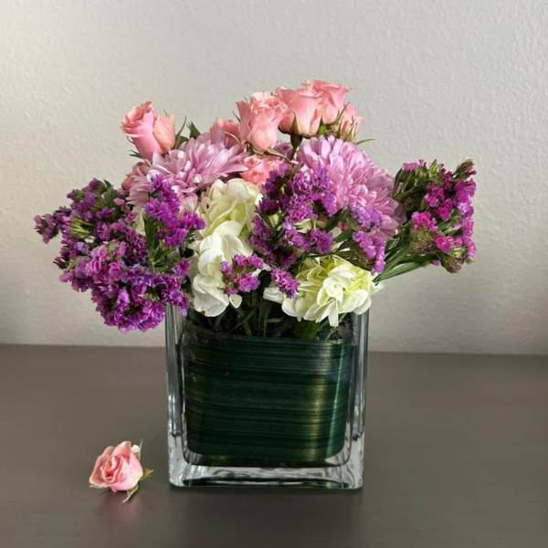 Pink roses and purple flowers arranged in a square glass vase