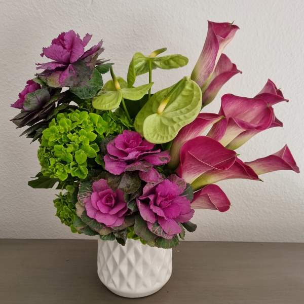 Pink calla lilies and purple ornamental cabbage in a white vase