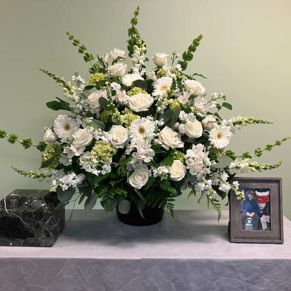 White floral arrangement in a black vase on a table with a framed photo