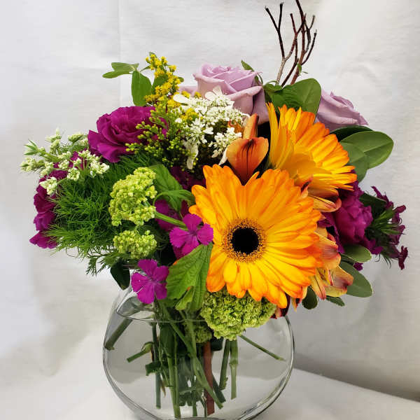 Mixed bouquet with orange gerbera daisies and lavender roses in a glass vase