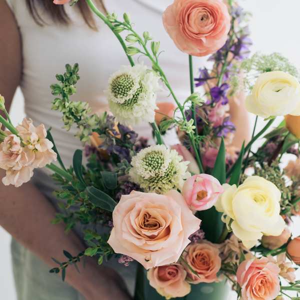 Handheld bouquet of peach, cream, and purple flowers