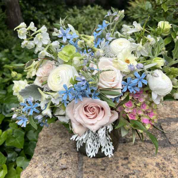 Mixed bouquet of pastel roses, white blooms, and blue flowers in a vase