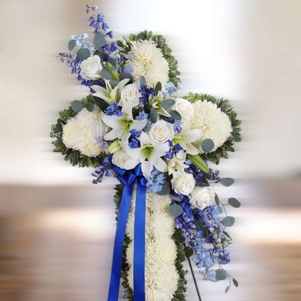 Standing cross of white mums with white lilies and roses, blue delphinium, and blue ribbon