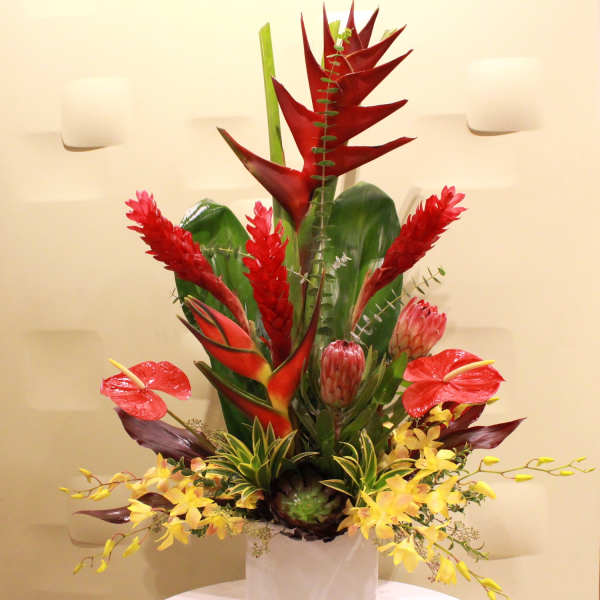 Tropical floral arrangement in a white vase with red and yellow blooms