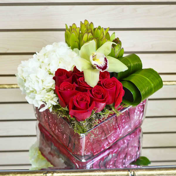 Red roses and white hydrangea in a pink gift box with green orchid petals