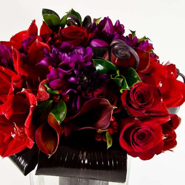 Red roses, purple flowers, and dark calla lilies in a black vase