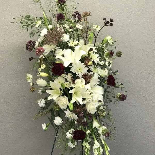 Tall white floral spray with lilies and mixed blooms on an easel