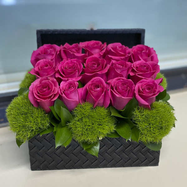 Pink roses arranged in a black woven box with green moss accents
