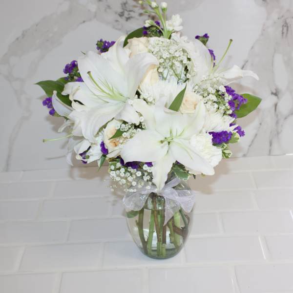 White lilies and roses in a glass vase with purple filler flowers