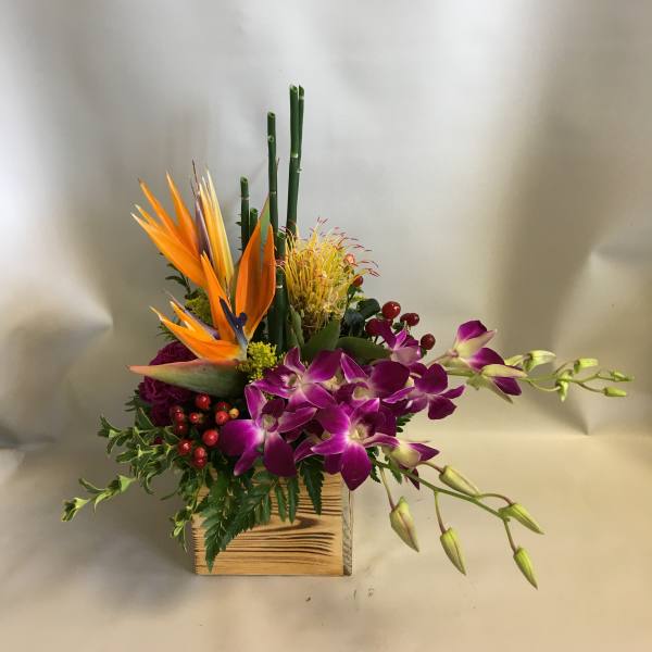 Tropical flower arrangement with purple orchids and orange bird-of-paradise in a wooden box