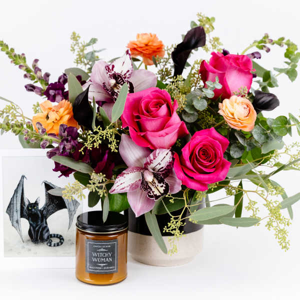 Mixed bouquet with pink roses and orchids in a vase beside a candle and framed bat print