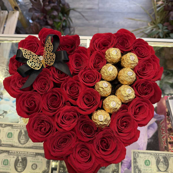Heart-shaped red rose arrangement with gold-wrapped chocolates and a black ribbon bow