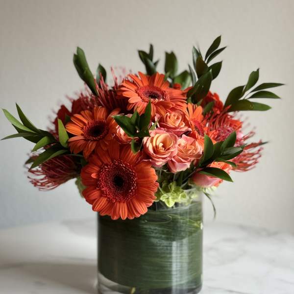 Orange gerbera daisies and peach roses in a glass vase