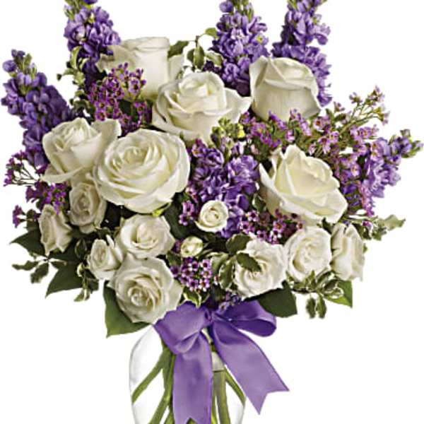 White roses and purple flowers in a clear glass vase with a purple ribbon