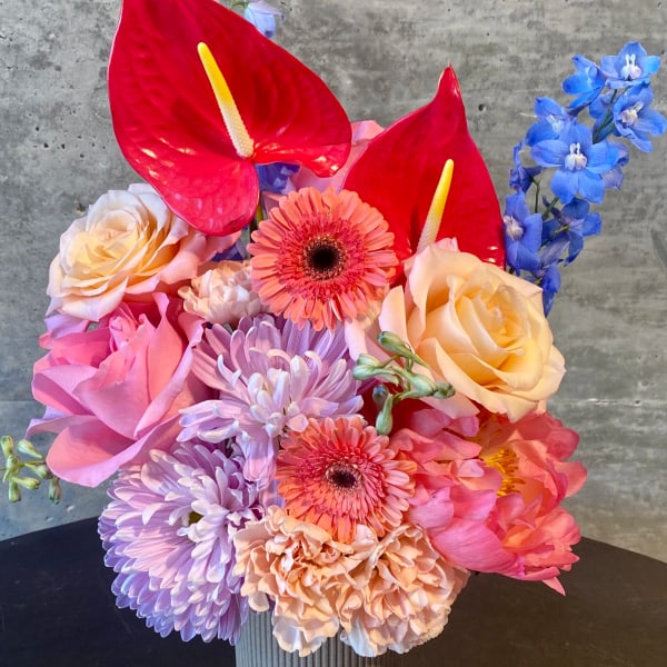 Colorful bouquet with roses, gerbera daisies, and red anthuriums in a ribbed vase