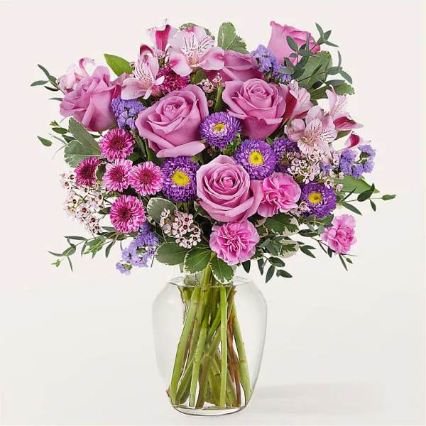 Mixed bouquet of pink roses, carnations, and purple asters in a clear glass vase