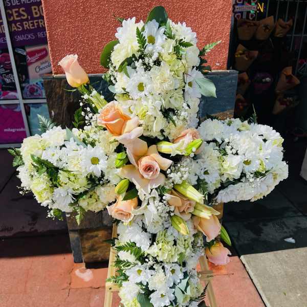 Large white floral cross with peach roses on a stand