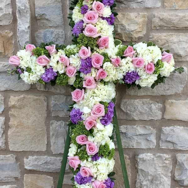 Floral cross arrangement with pink roses, white hydrangeas, and purple blooms