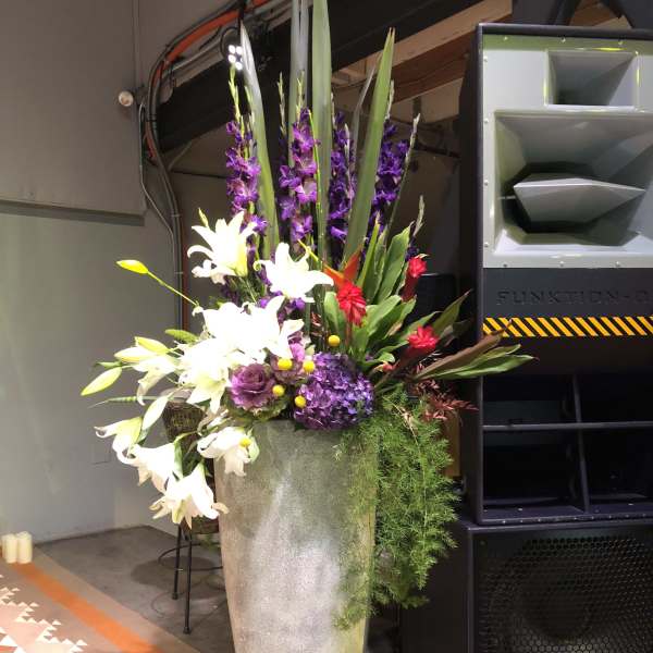 Tall floral arrangement in a silver vase with white lilies and purple blooms