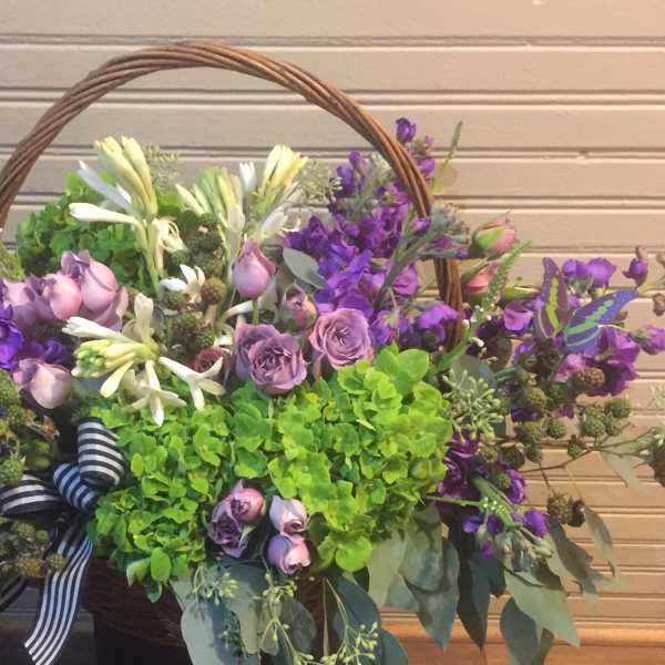 Basket arrangement of purple and white flowers with a striped ribbon