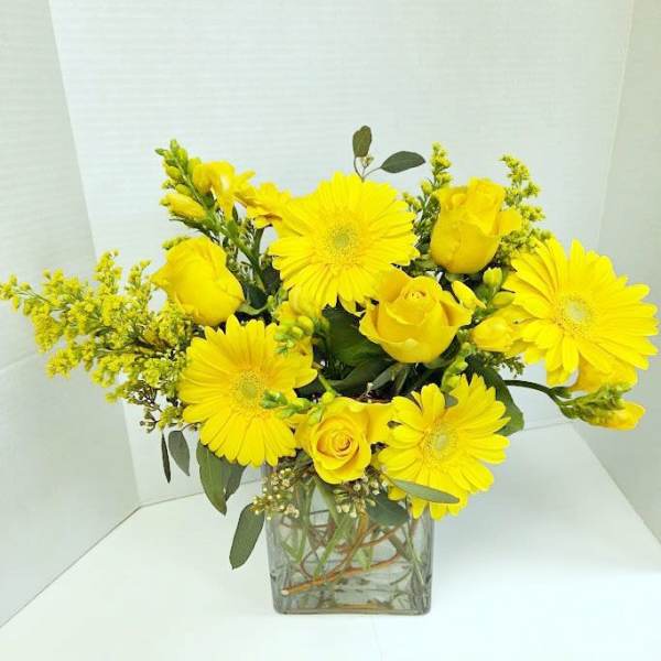 Yellow roses and gerbera daisies in a square glass vase
